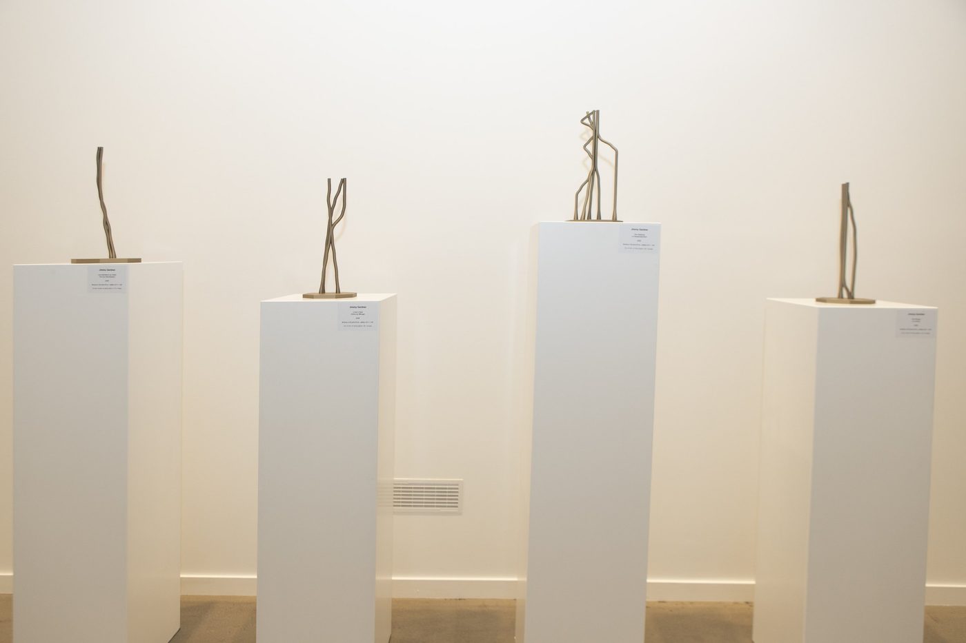 Four slender sculptures on white plinths.