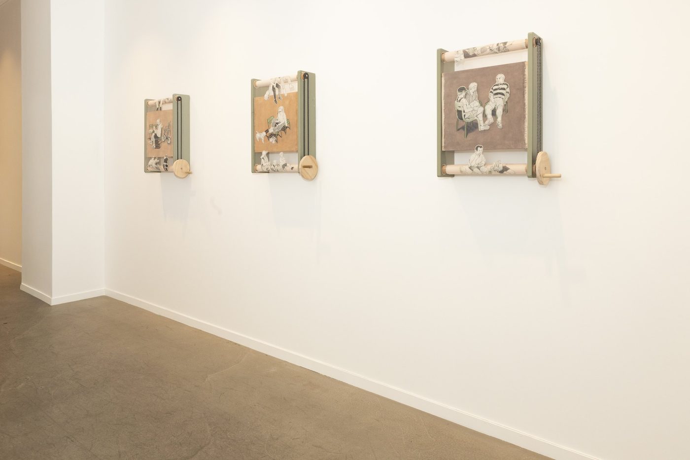 Three wall-mounted kinetic scrolls with wooden rollers and cranks.